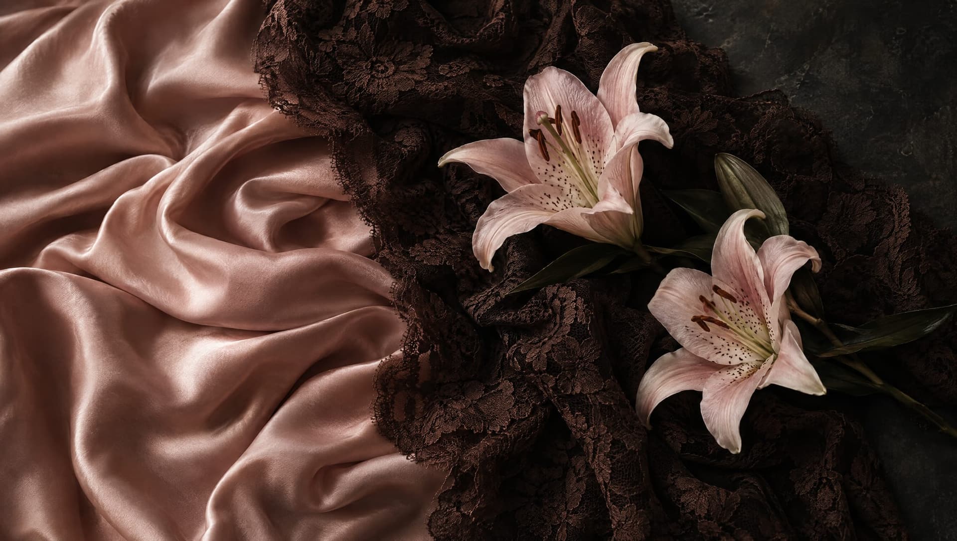 Zwei rosa Lilien auf rosé Satin und dunkelbrauner Spitze.